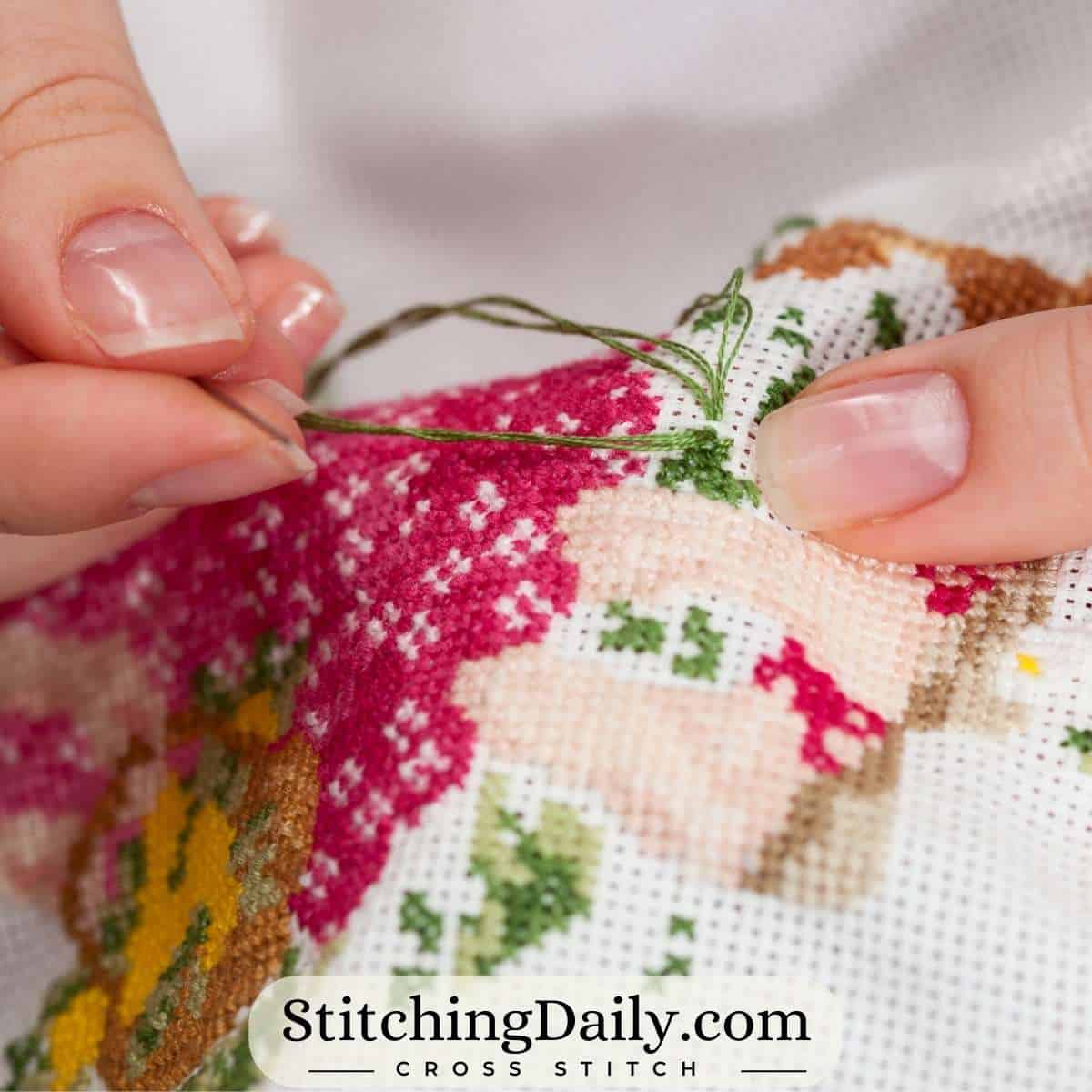 Person cross stitching on white Aida using 2 strands of embroidery floss